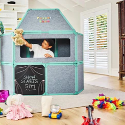 Children playing with a playhouse in a room with toys scattered around.